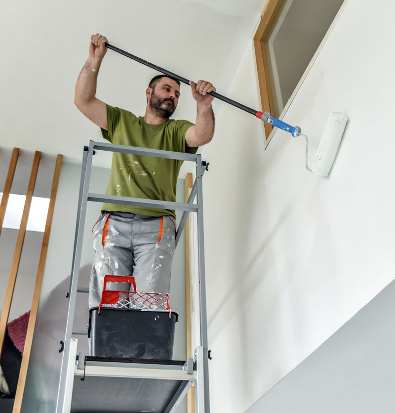 Professional painter painting a large room standing on some scaffolding